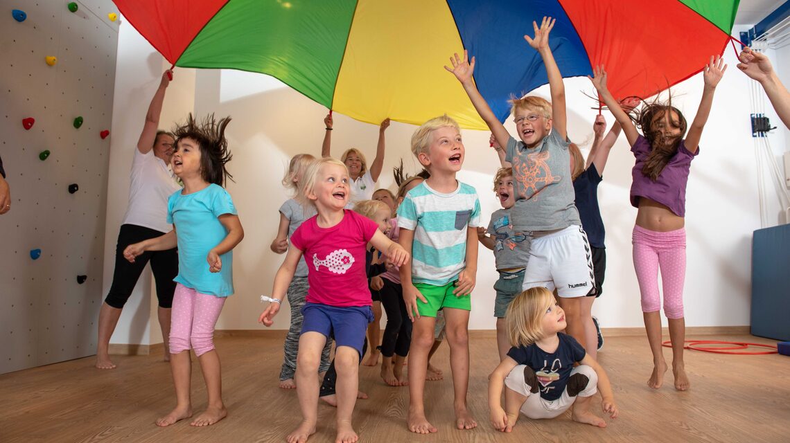 Kindergruppe springt jubelnd unter dem bunten Schwungtuch bei SportStart Ottensen